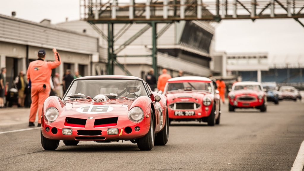 3 red classic racing cars in pit lane