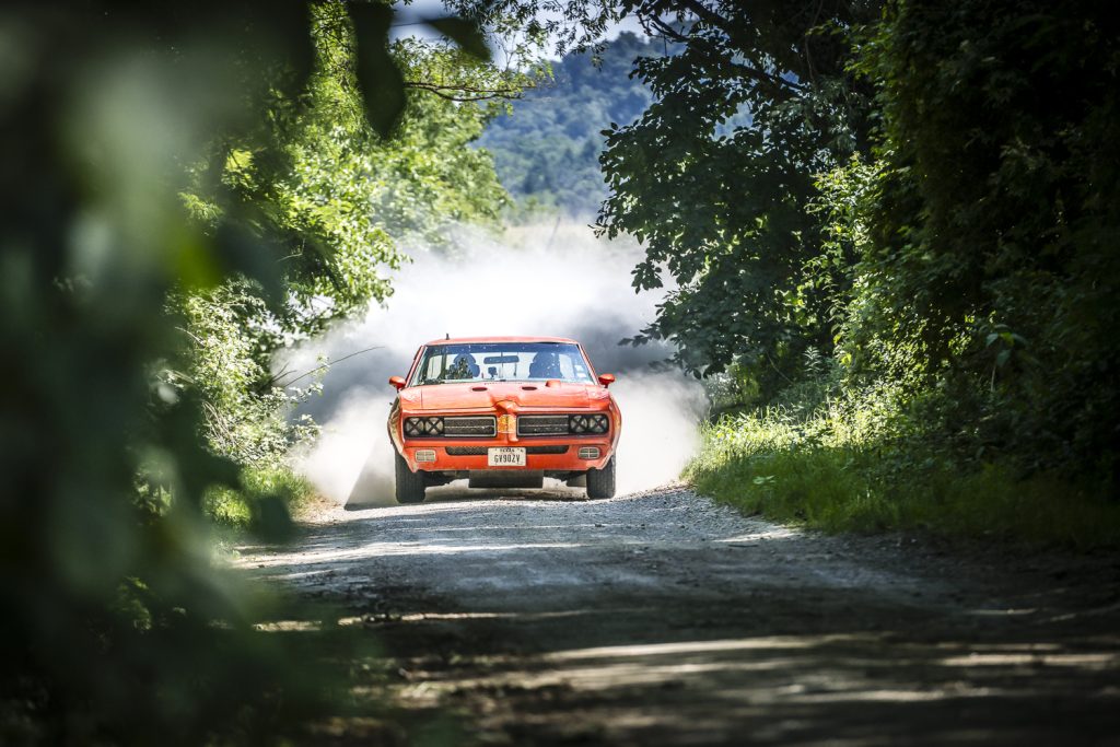 red dodge drives on dusty track through trees