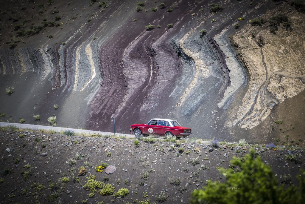 red volvo drives past coloured rock strata